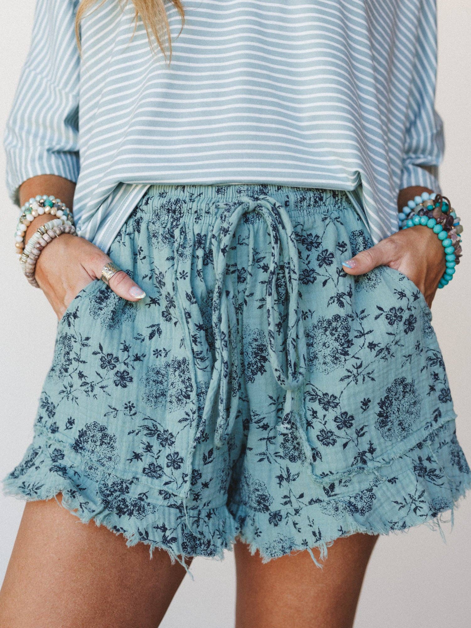 Person wearing a striped shirt and floral shorts with bracelets on a neutral background