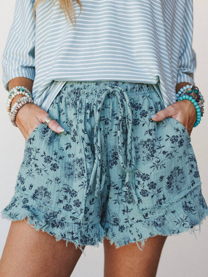 Person wearing a striped shirt and floral shorts with bracelets on a neutral background