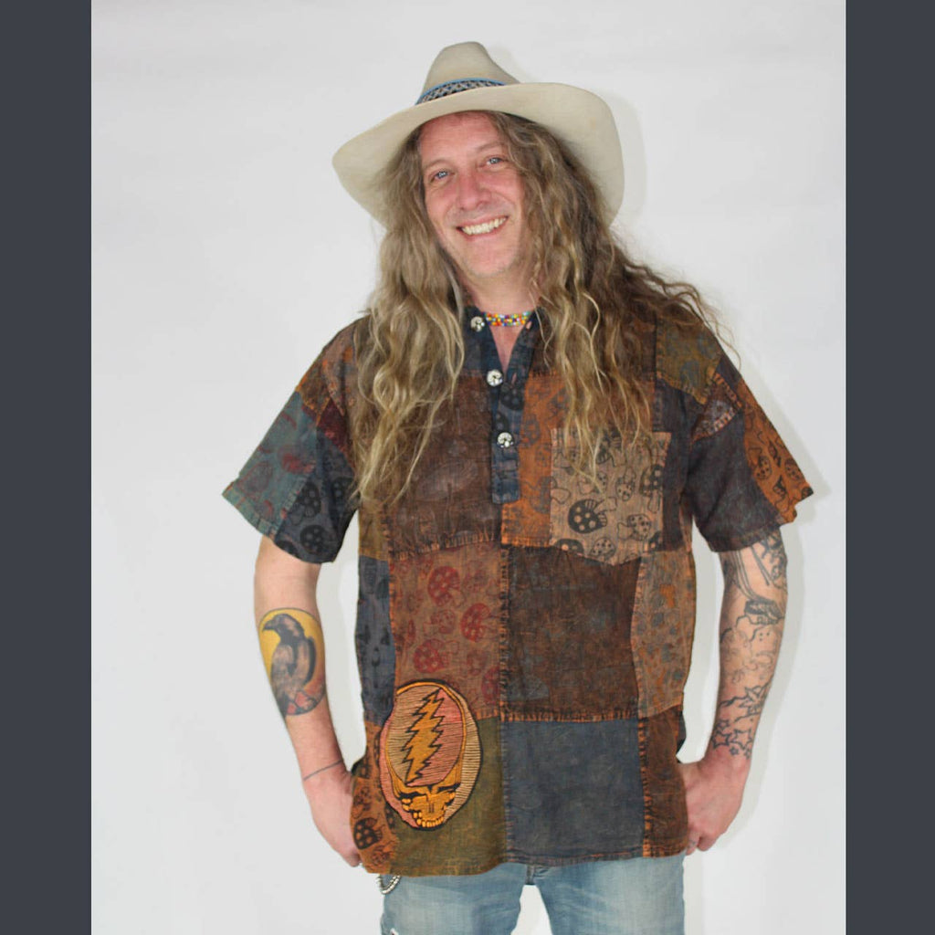 Person wearing a patchwork shirt with a visible band logo on a plain background
