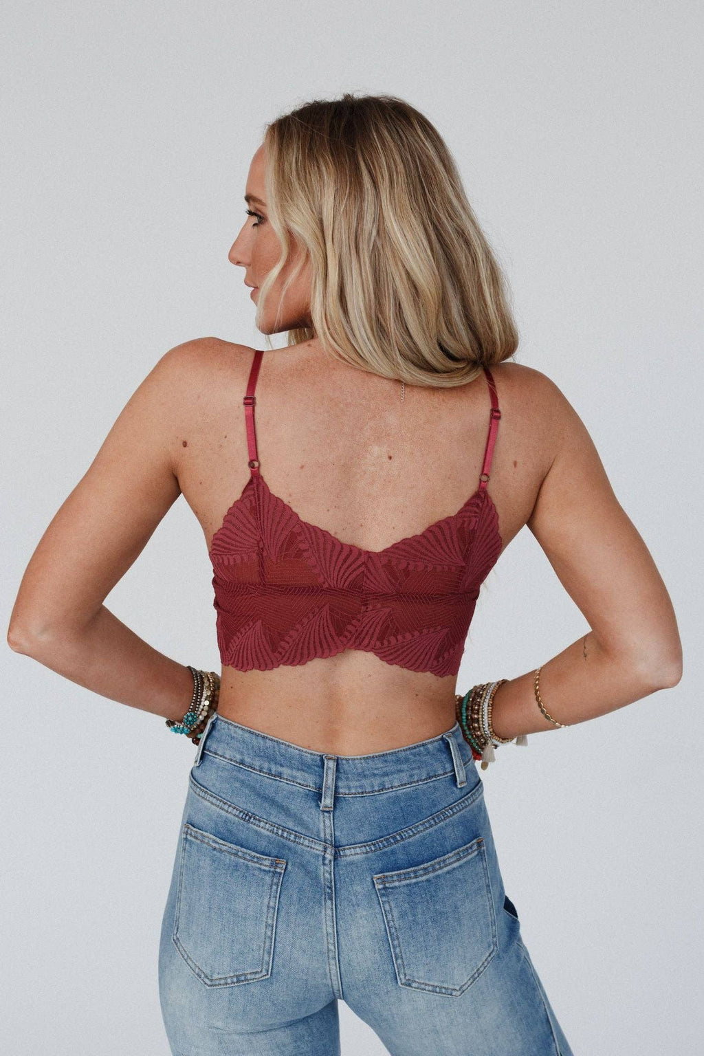 Woman wearing a red lace top and blue jeans against a plain background