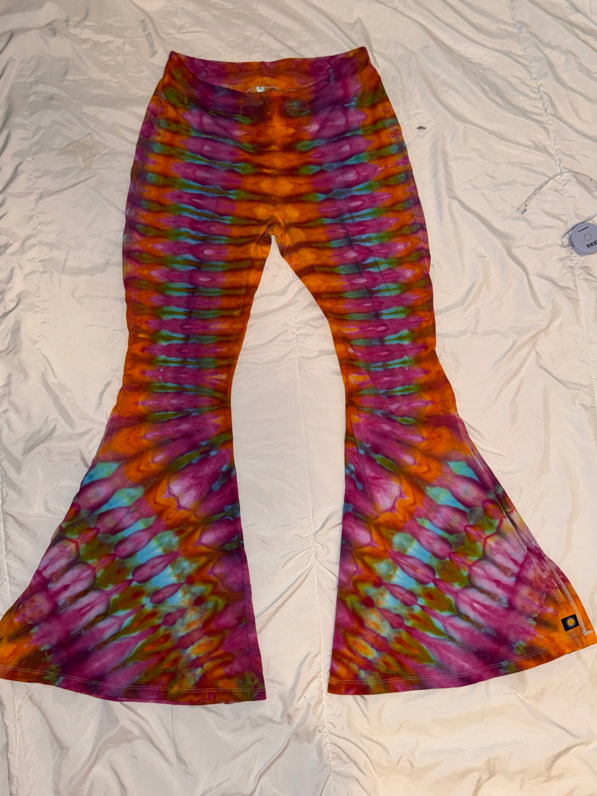 Cosmic Bloom Bellbottoms close-up — vibrant tie-dye swirl fabric in purple, blue, and warm tones, wide-leg rave flare pants